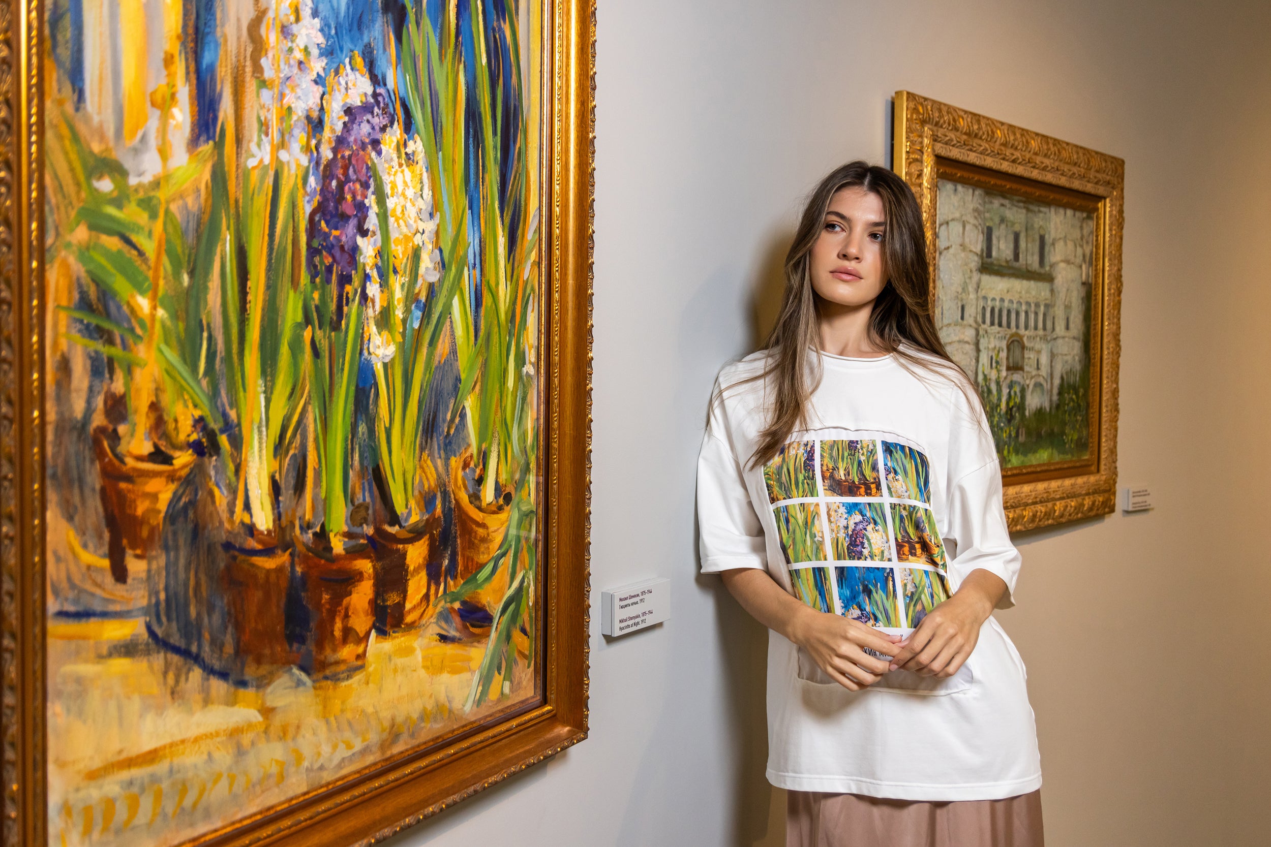 Woman standing in an art gallery wearing a white t-shirt with colorful design, surrounded by Van Gogh paintings.