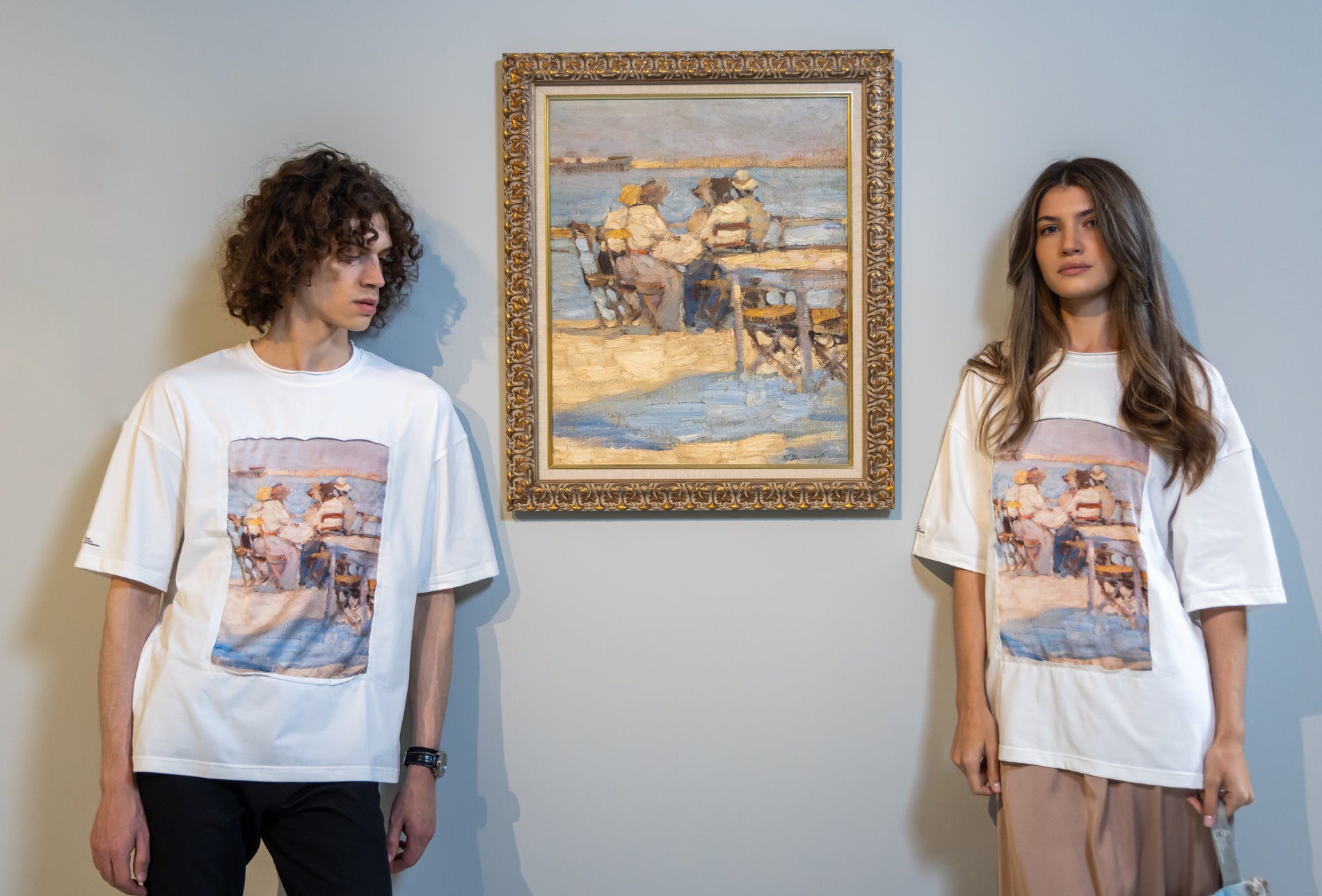 Two people wearing t-shirts with artistic prints in front of a framed painting.
