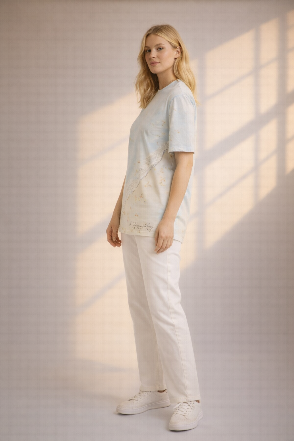 Woman wearing a light blue t-shirt and white pants standing in a softly lit room.