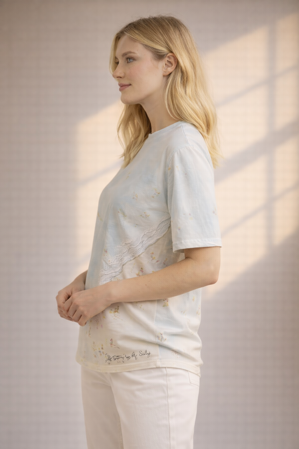 Woman wearing a light-colored top and pants standing in a softly lit room.