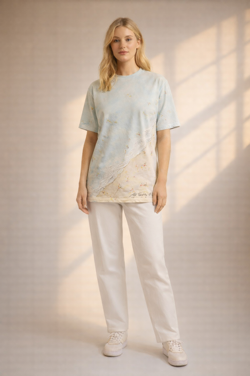 Woman wearing a light blue t-shirt with a graphic design and white pants in a softly lit room.