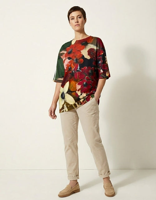 Person wearing a colorful floral top and beige pants on a white background