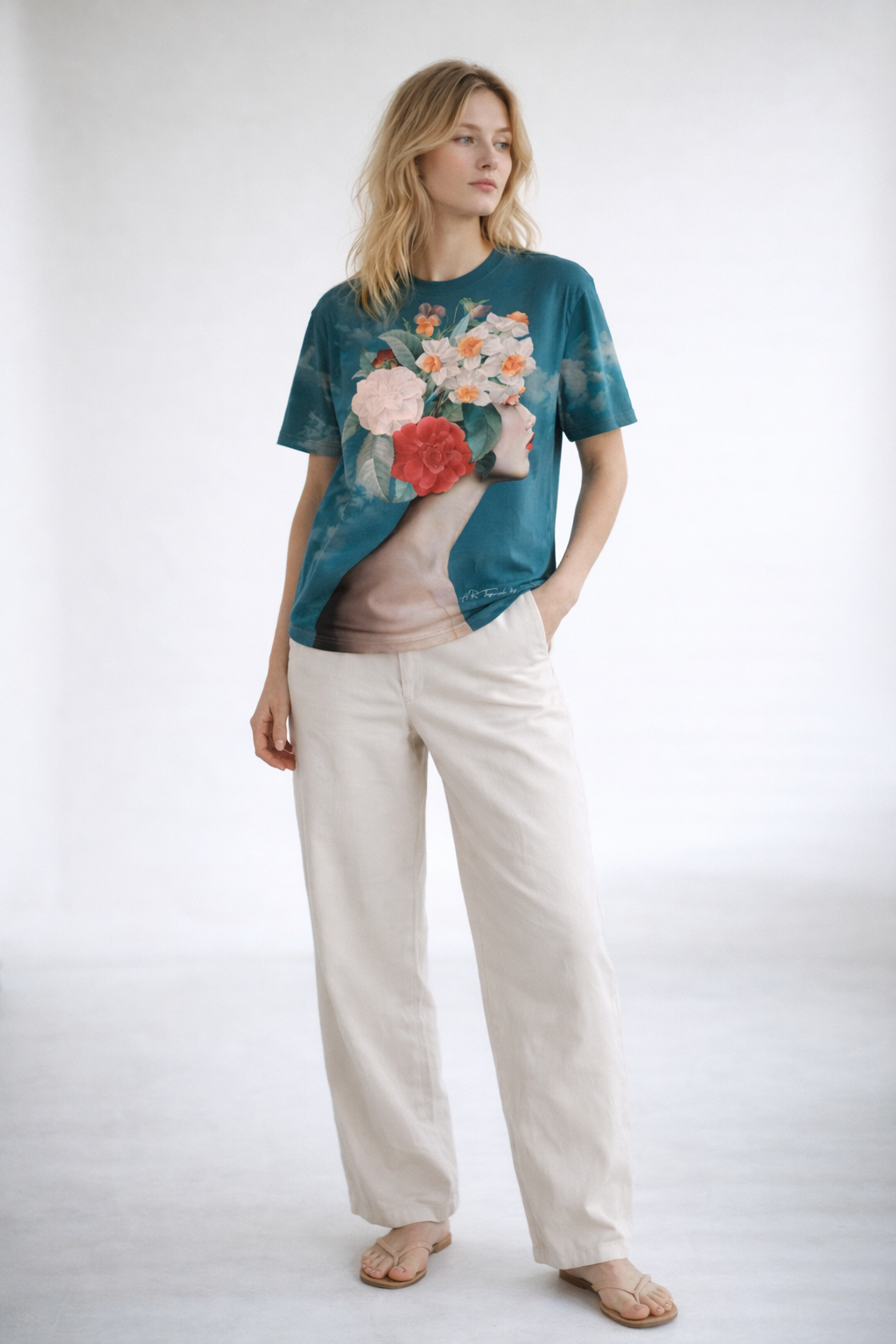 Woman wearing a teal t-shirt with floral design and beige pants on a white background