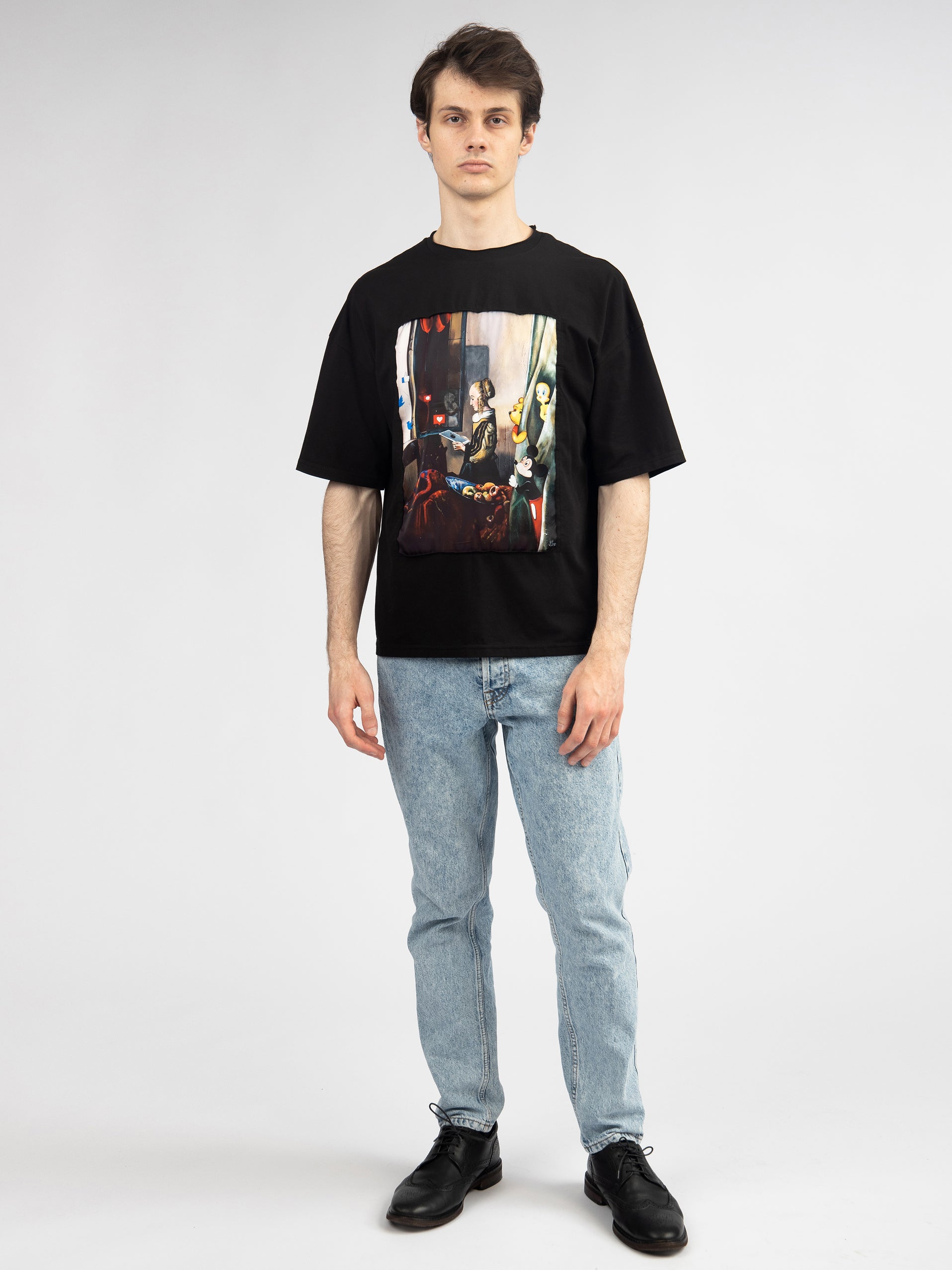 Person wearing a black t-shirt with a graphic design and light blue jeans on a white background