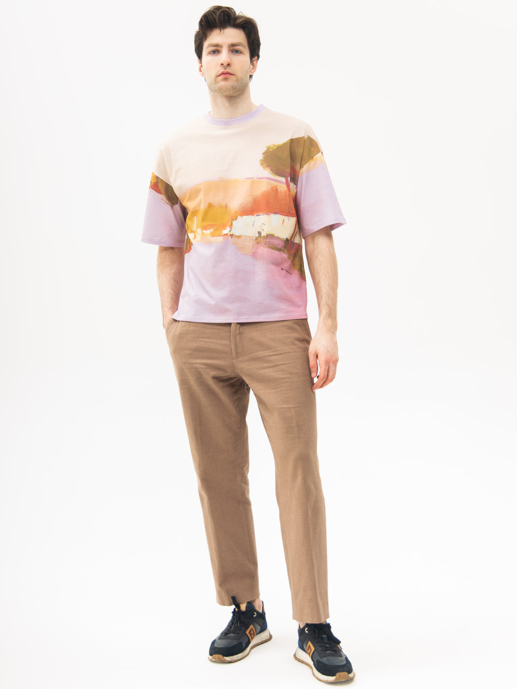 Man wearing a colorful t-shirt with landscape and beige pants on a white background