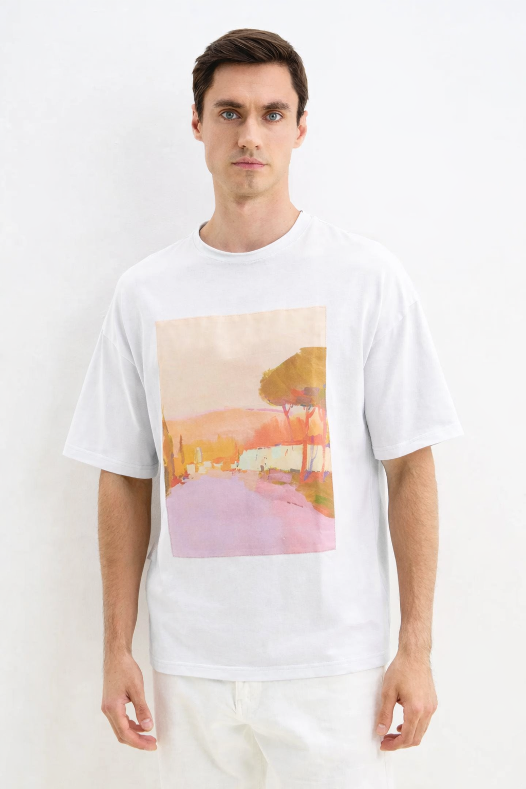 Man wearing a white t-shirt with a colorful landscape design on a plain background