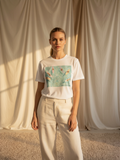 Woman wearing a white t-shirt with a colorful graphic design against a neutral curtain background