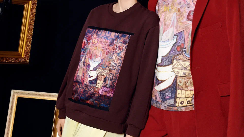 Mannequin wearing a brown sweatshirt with a colorful graphic design, standing next to a red garment.